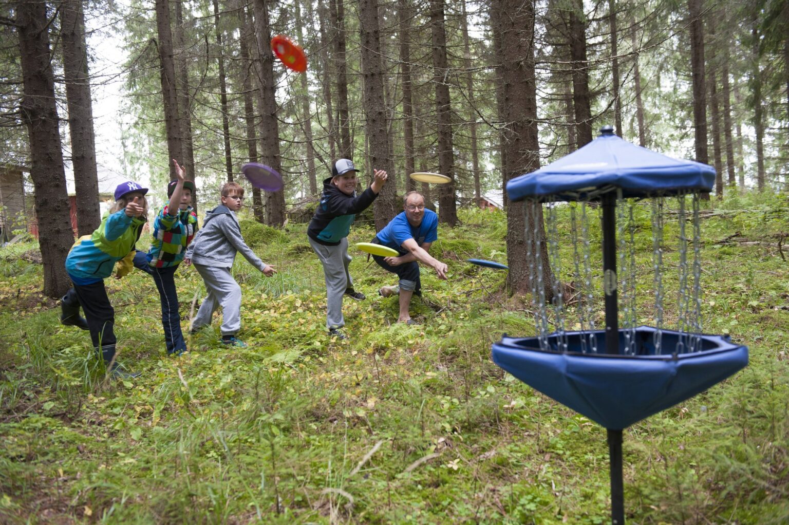 Kuvituskuva. Nuoret heittävät frisbeetä koriin.